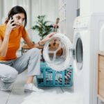 Donna al telefono con lavatrice che perde schiuma