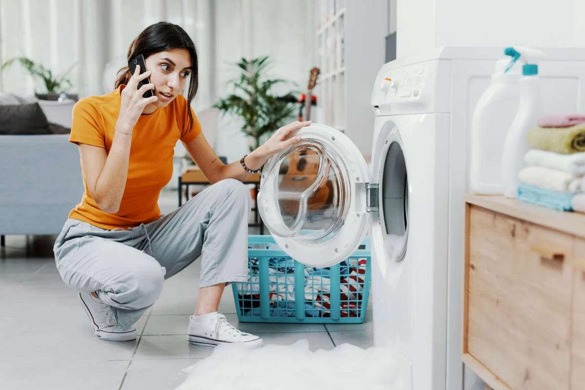 Donna al telefono con lavatrice che perde schiuma