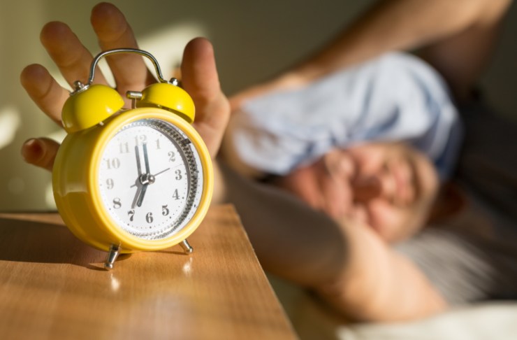 uomo a letto che spegne la sveglia