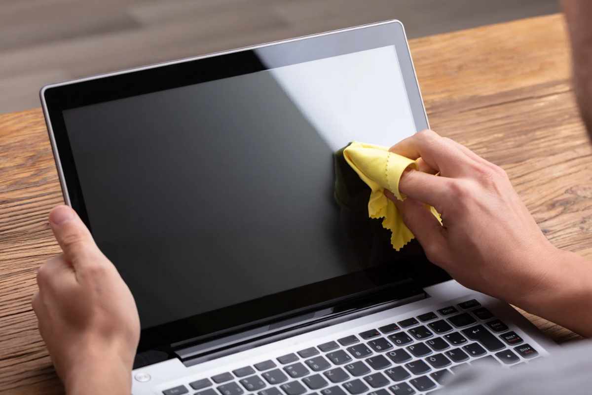 Persona che pulisce schermo PC portatile